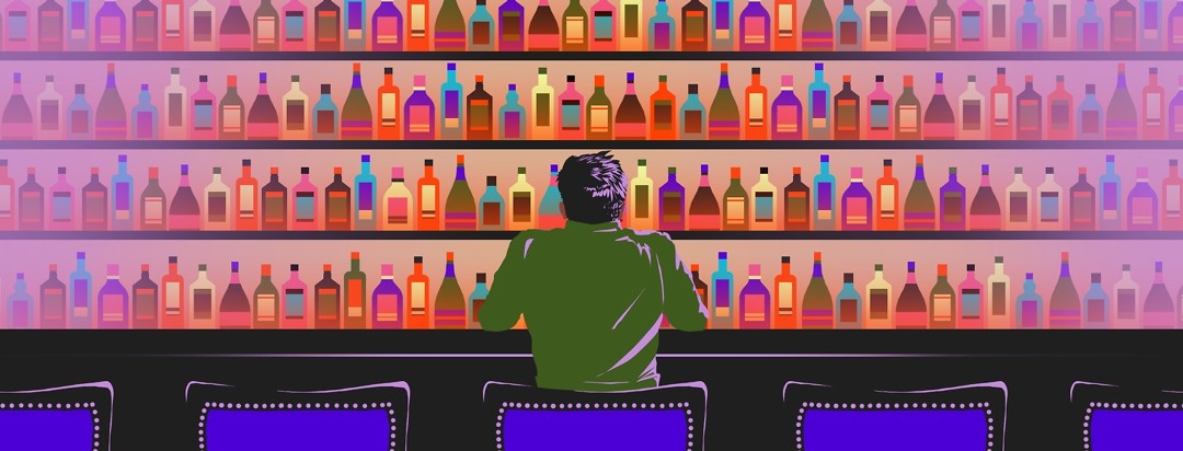 A man sits at a bar, staring at the shelves of alcohol in front of him.